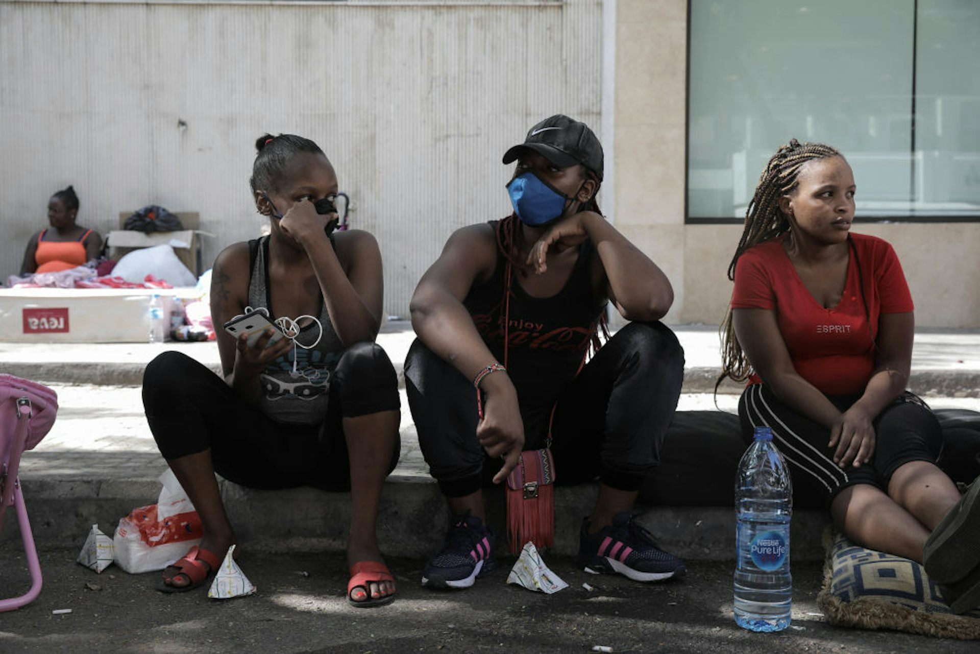 Three young women seated side by side on a street pavement 