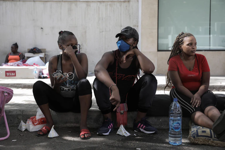 Three young women seated side by side on a street pavement