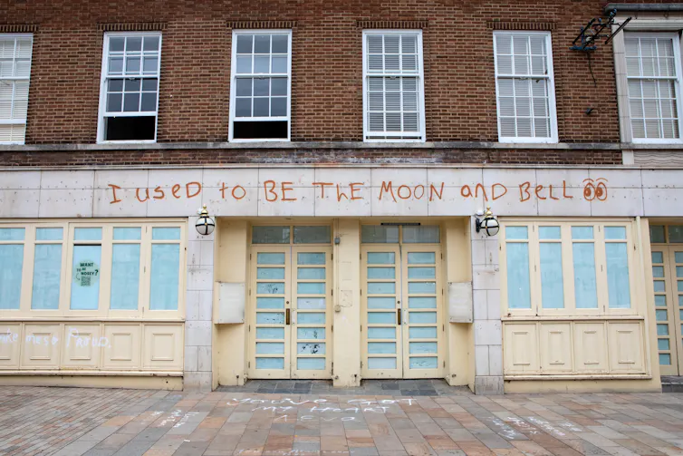 A boarded-up pub with graffiti across the top reading 'I used to be the moon and bell'