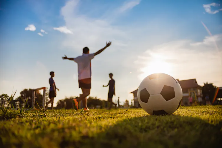 Photo focused on a football sitting on grass while players celebrate in the background