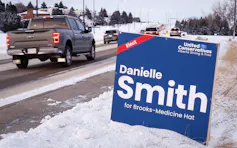 El camión pasa el letrero de Danielle Smith al lado de la carretera nevada.