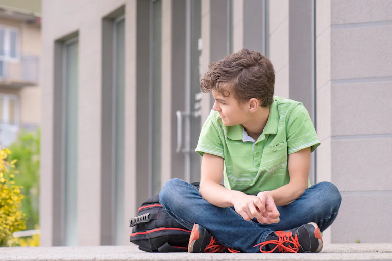 Boy with school bag sitting cross legged outside