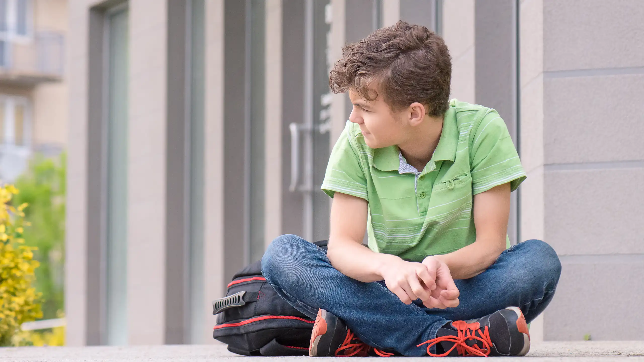 Boy with school bag sitting cross legged outside