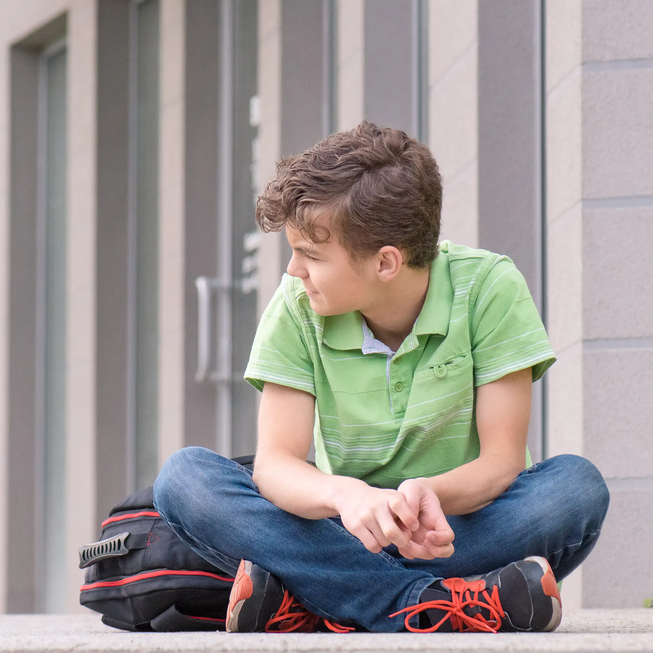 Boy with school bag sitting cross legged outside