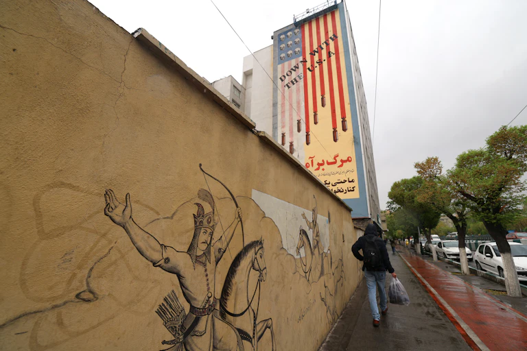 A man walks past a large paining on a building.