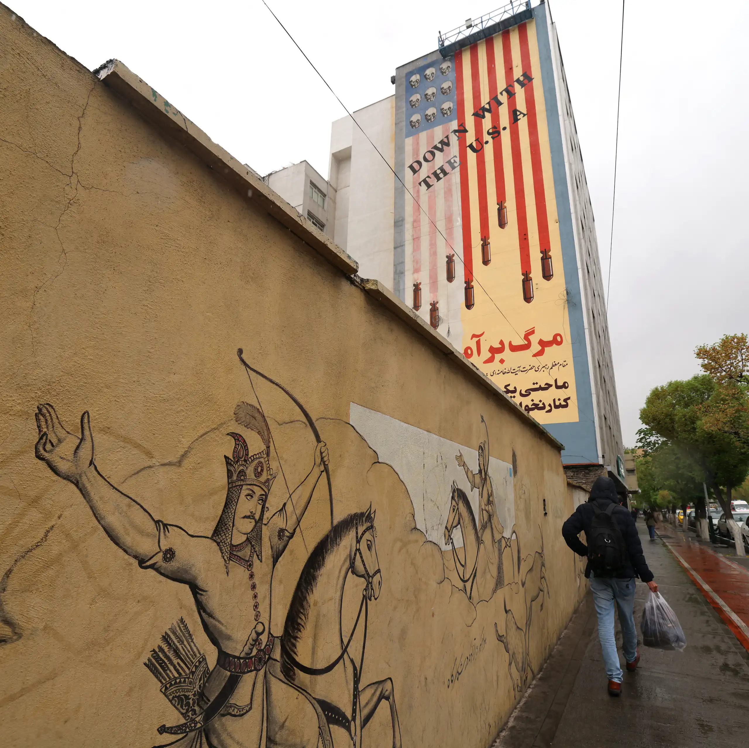 A man walks past a large paining on a building.