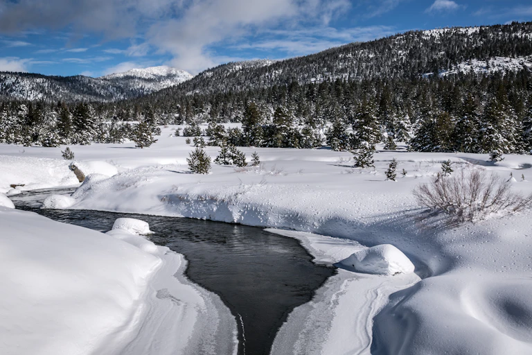 A few across a mountain stream near Lake Tahoe and land covered in snow.