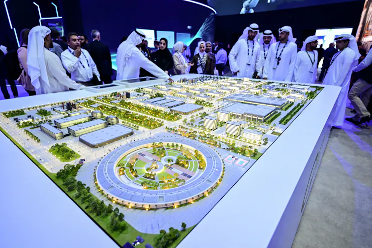 men wearingwhite robes and headdresses stand over a model of an industrial park