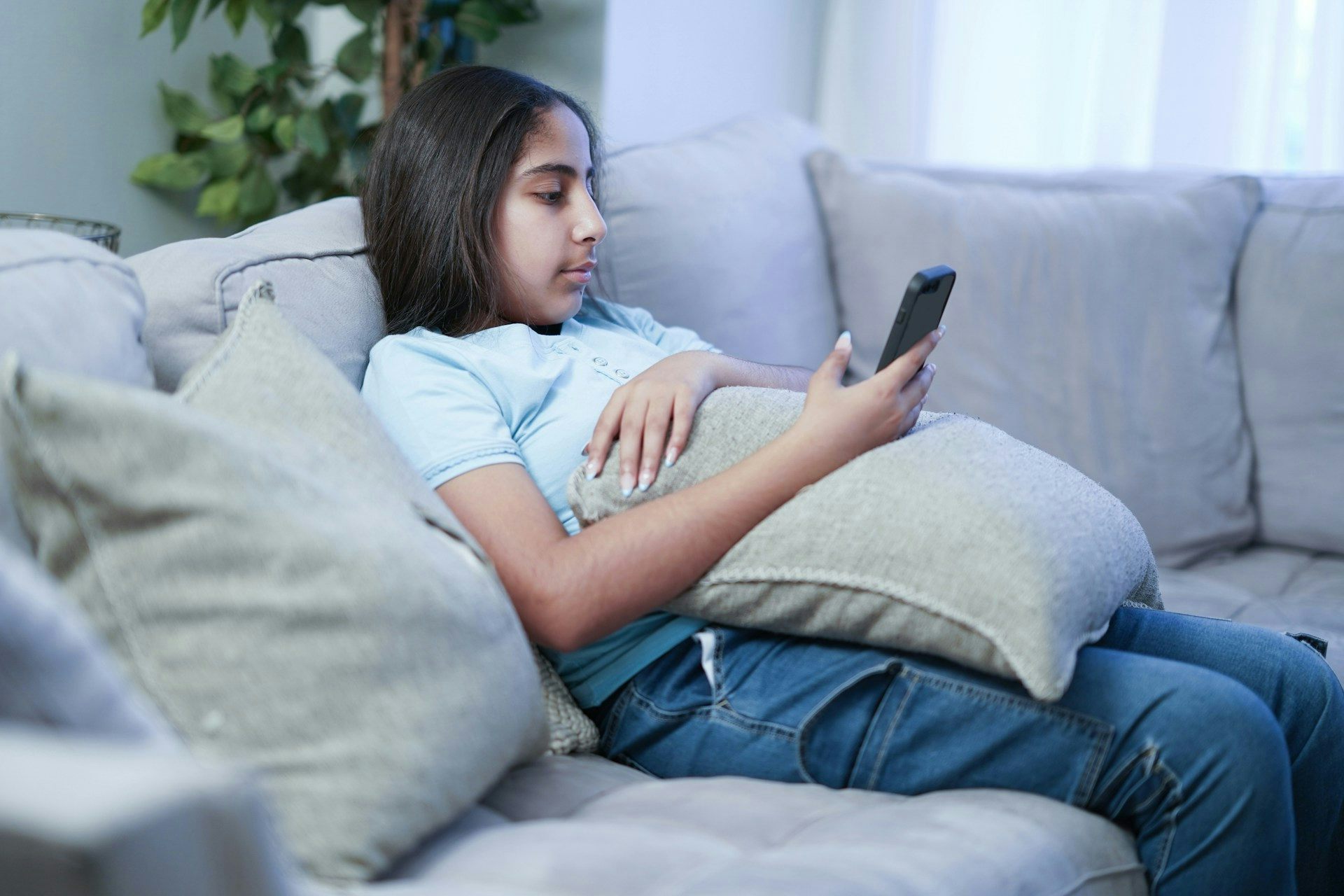 Una adolescente acurrucada en el sofá y mirando su teléfono inteligente.