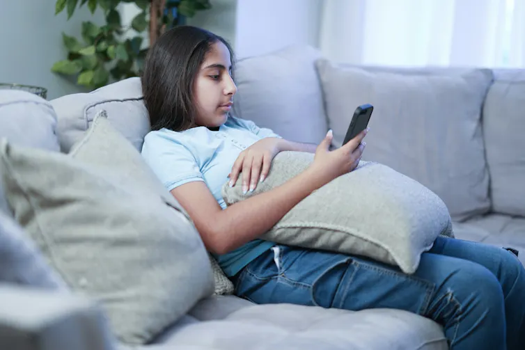 Una adolescente acurrucada en el sofá y mirando su teléfono inteligente.