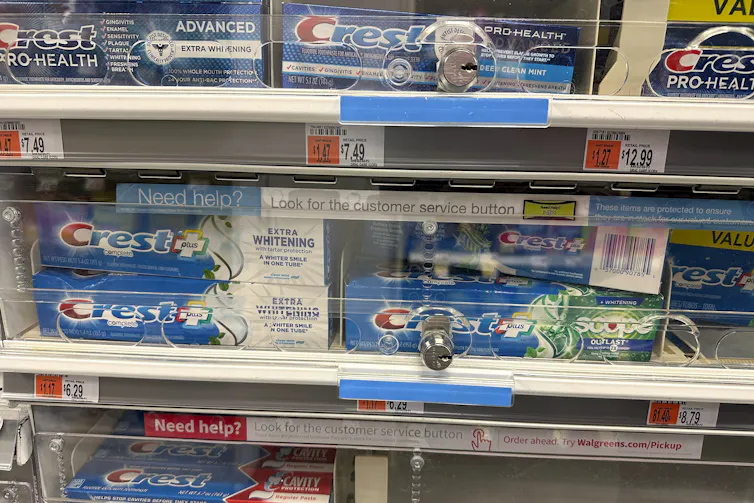 Tubes of toothpaste are displayed behind a locked, plastic barrier