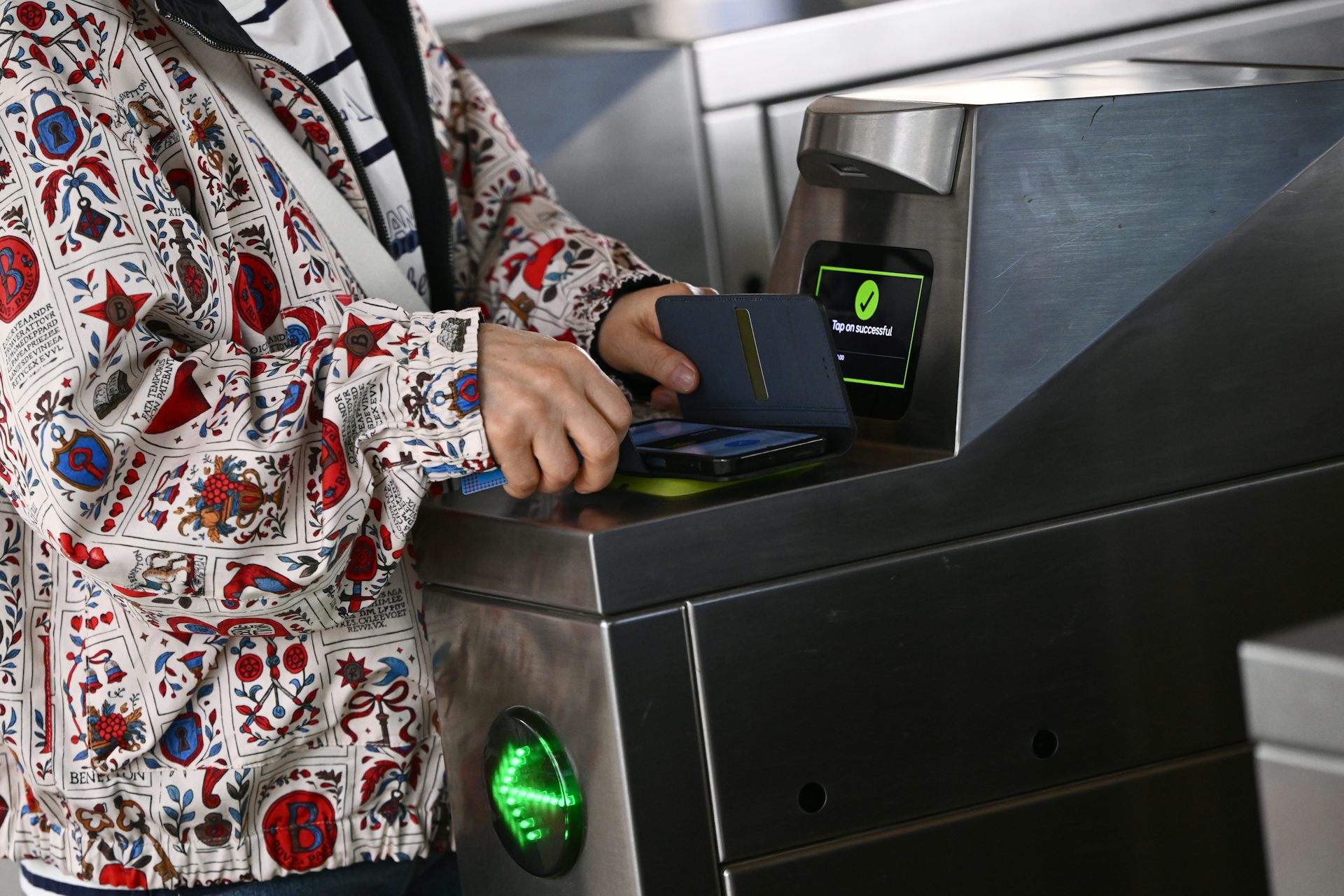 A woman's hands holds a phone over a ticket scanner at a train station turnstile.