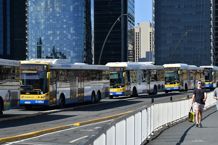 A series of busses driving along a busy city road.