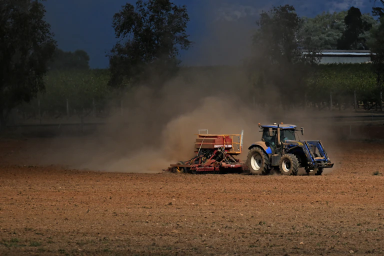 A tractor ploughs a dusty orange field.