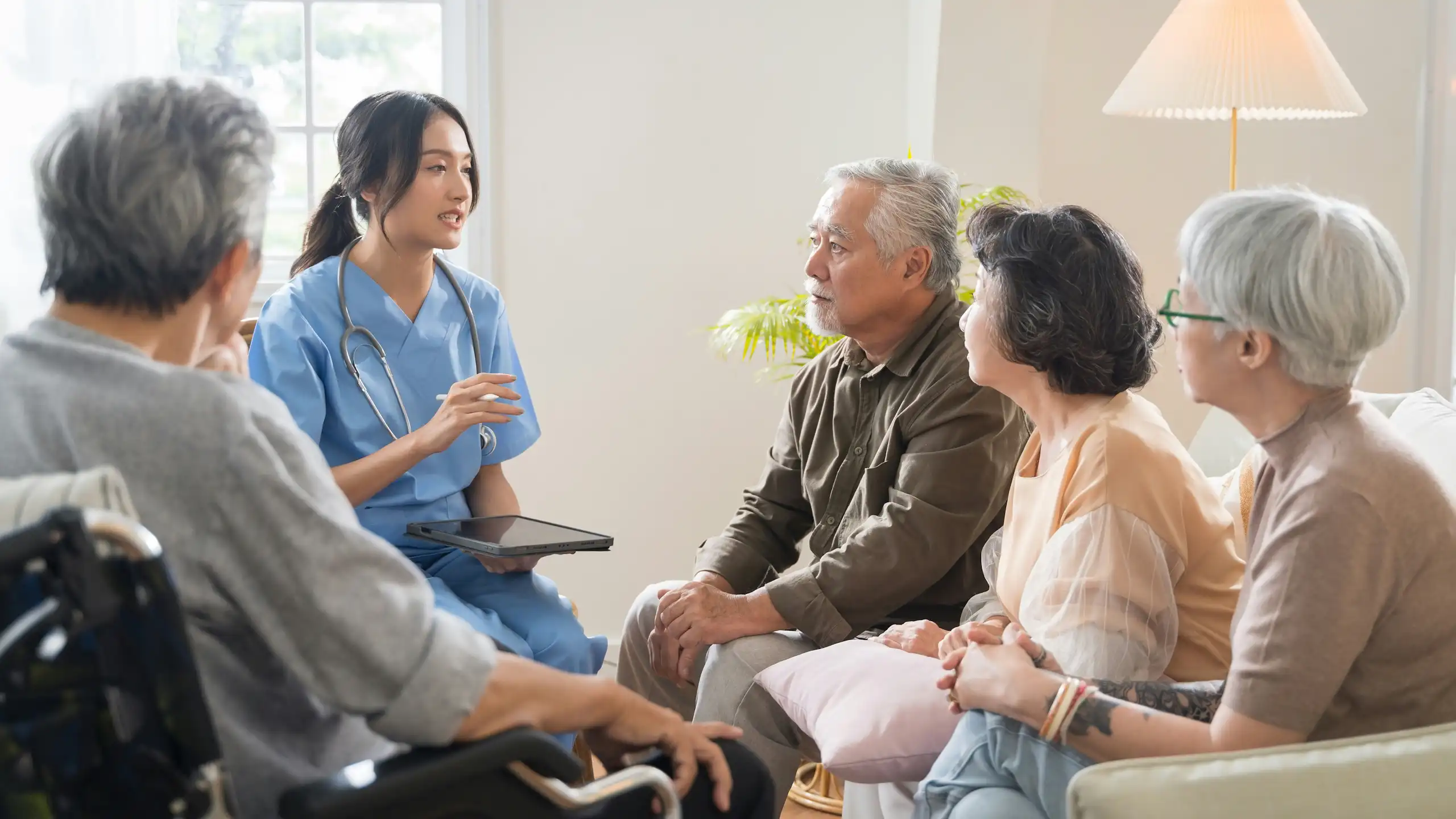 A group of older adults and a younger woman in scrubs with a stethoscope and clipboard