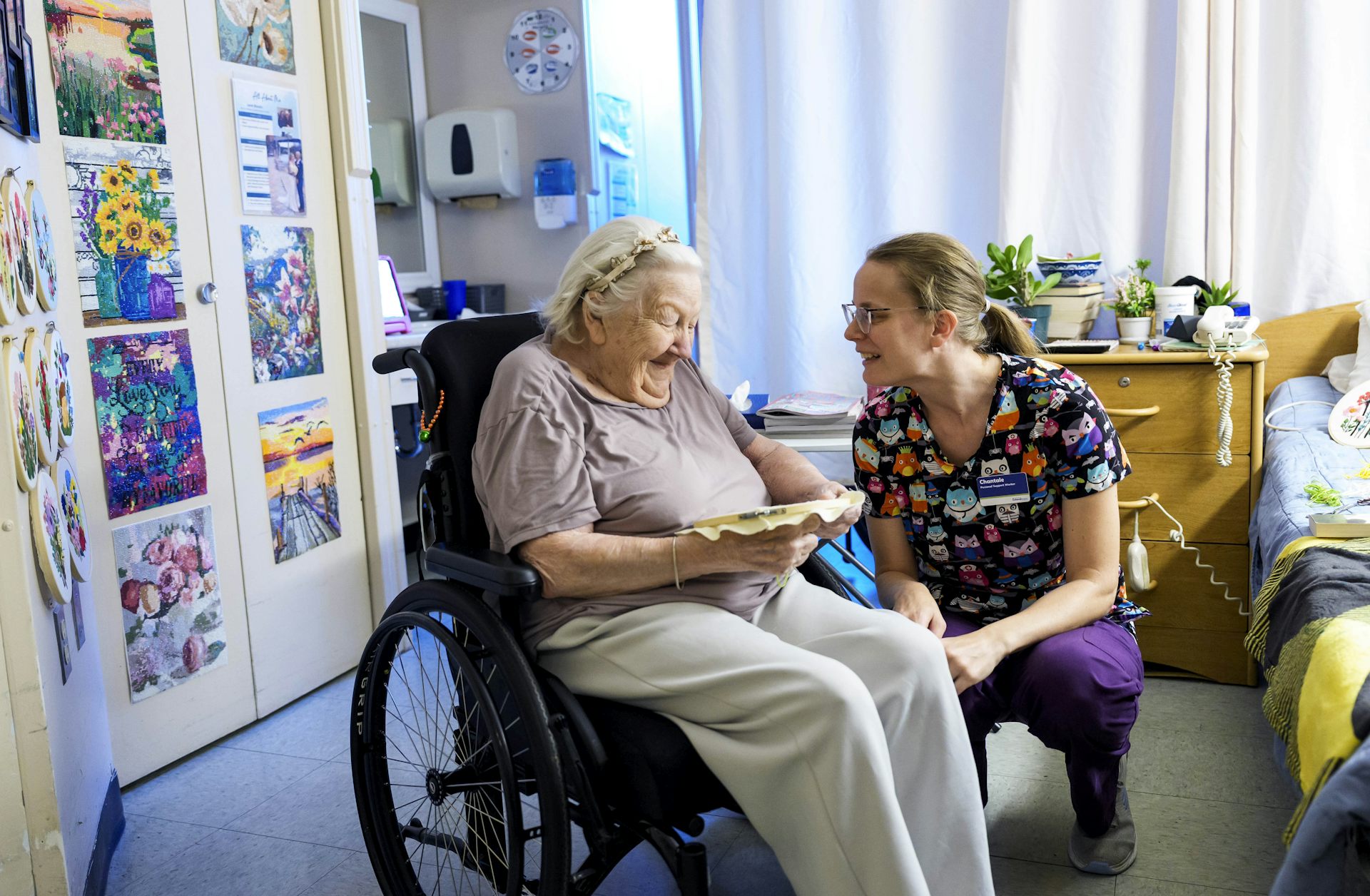 Una mujer en bata habla con una mujer con cabello gris sentada en una silla de ruedas