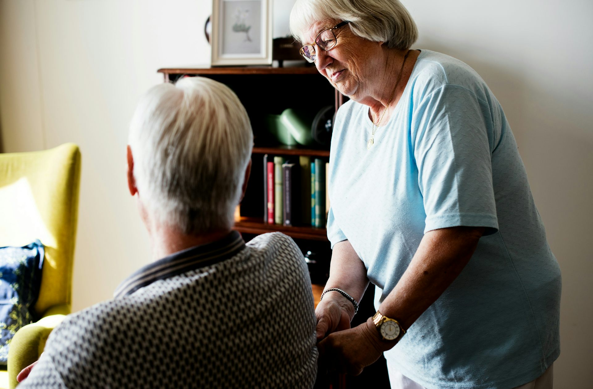 Una anciana habla con un hombre sentado con el pelo gris visible desde atrás.