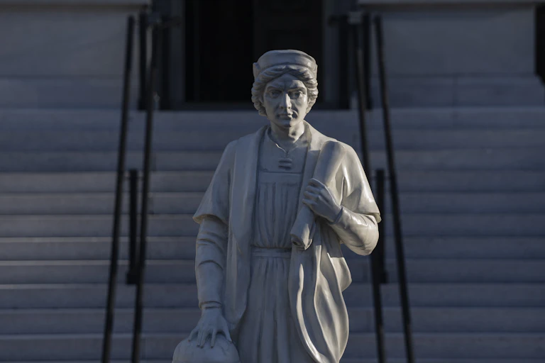 Statue of a man holding a scroll, with stairs in the background