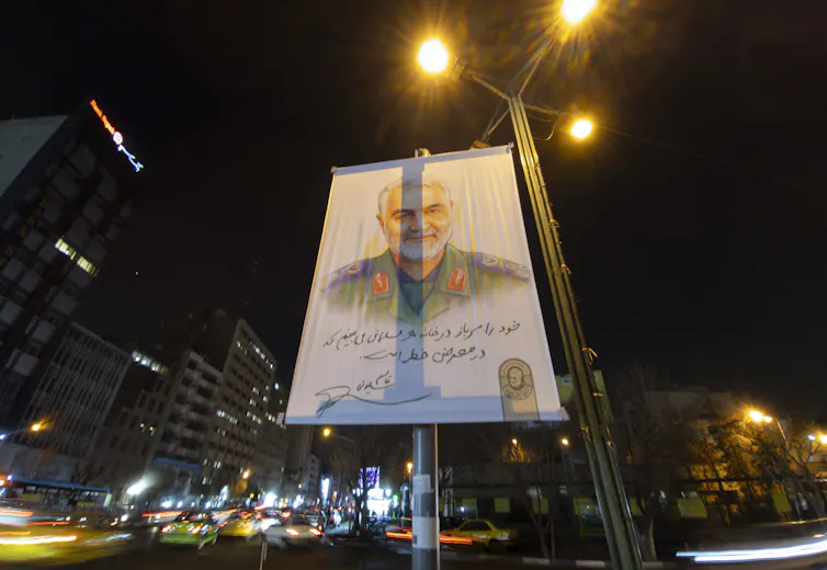 A large billboard seen at night has a man's face on.