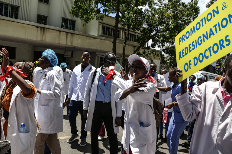 A group of people in white coats, in the street, some holding posters, some blowing whistles