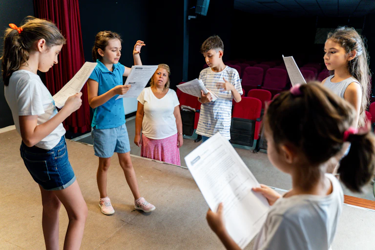 A group of children read scripts on a stage.
