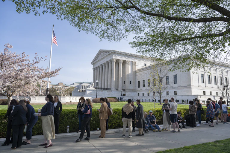 People stand in line on sunny day outside the U.S. Supreme Court building.
