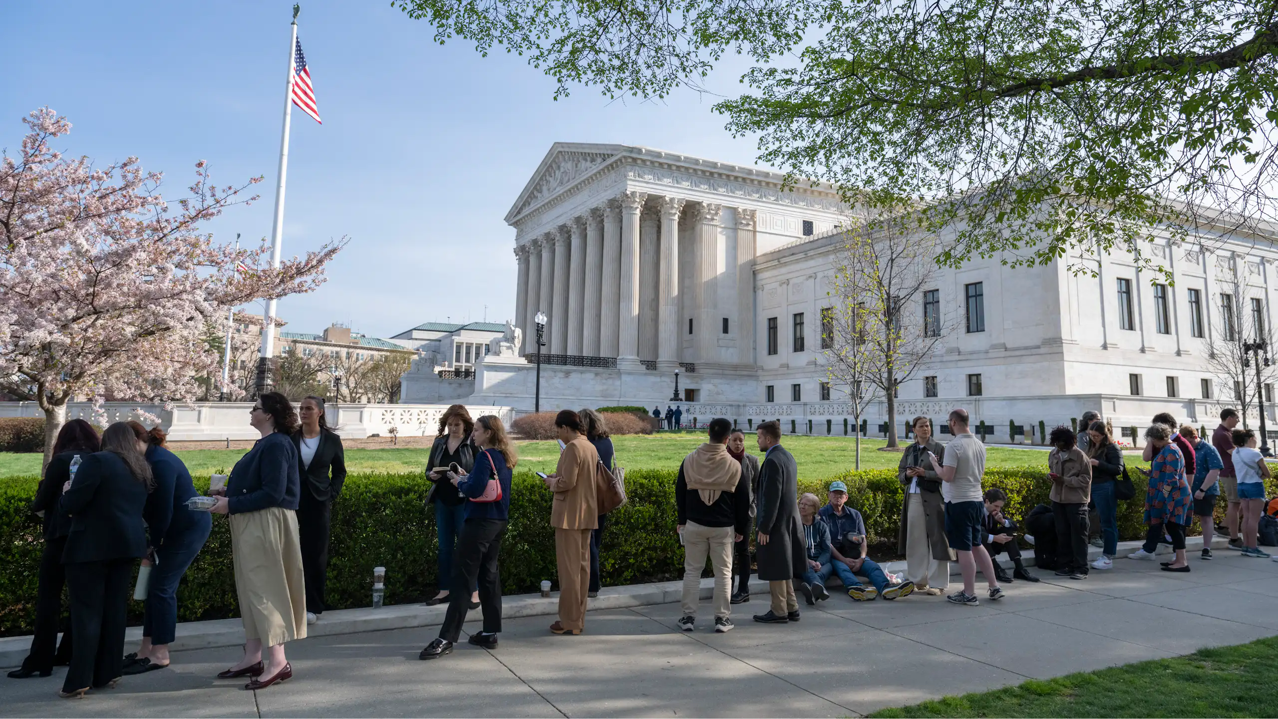 People stand in line on sunny day outside the U.S. Supreme Court building.