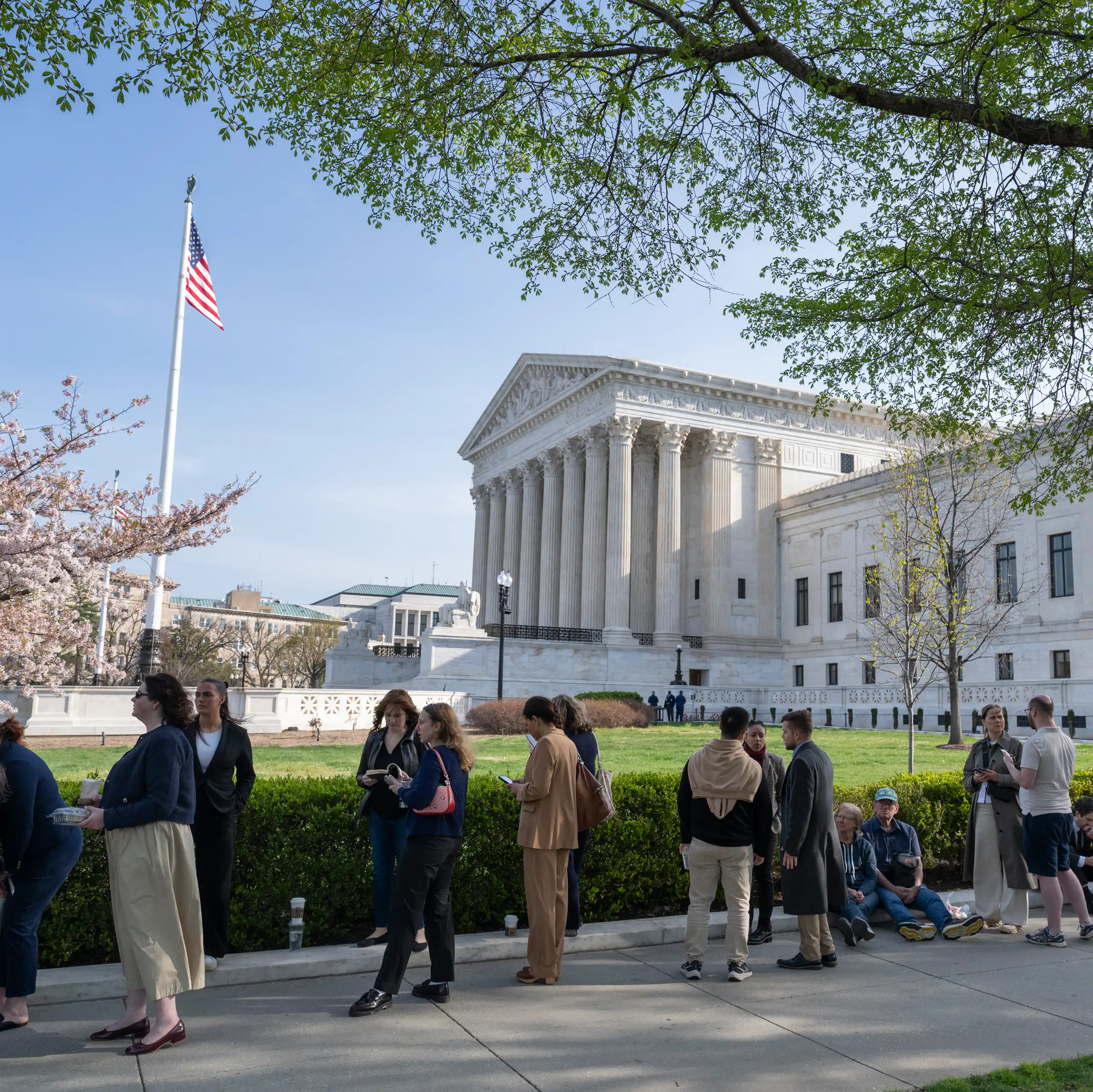 People stand in line on sunny day outside the U.S. Supreme Court building.