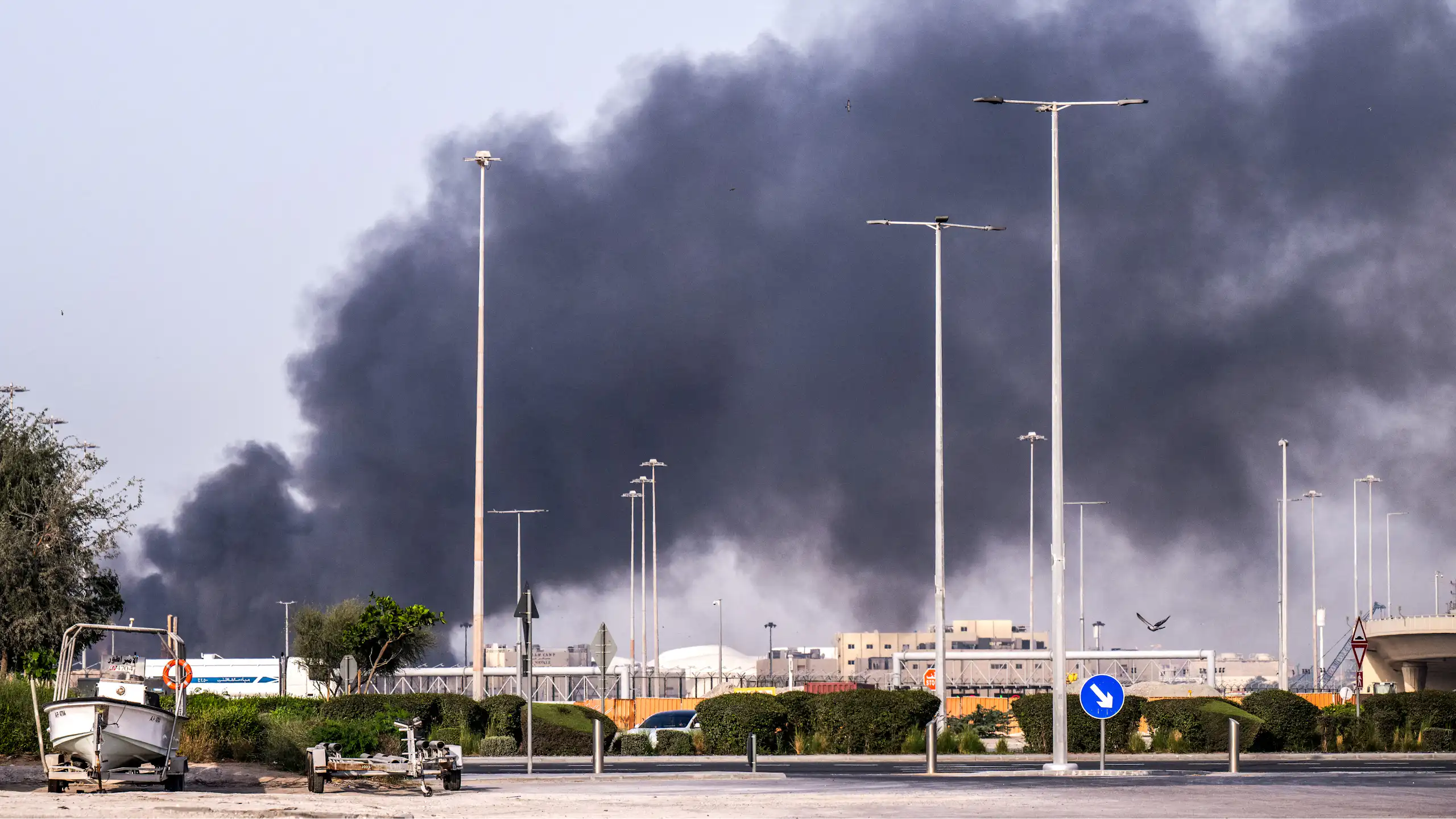 a large plume of black smoke rises in an industrial area