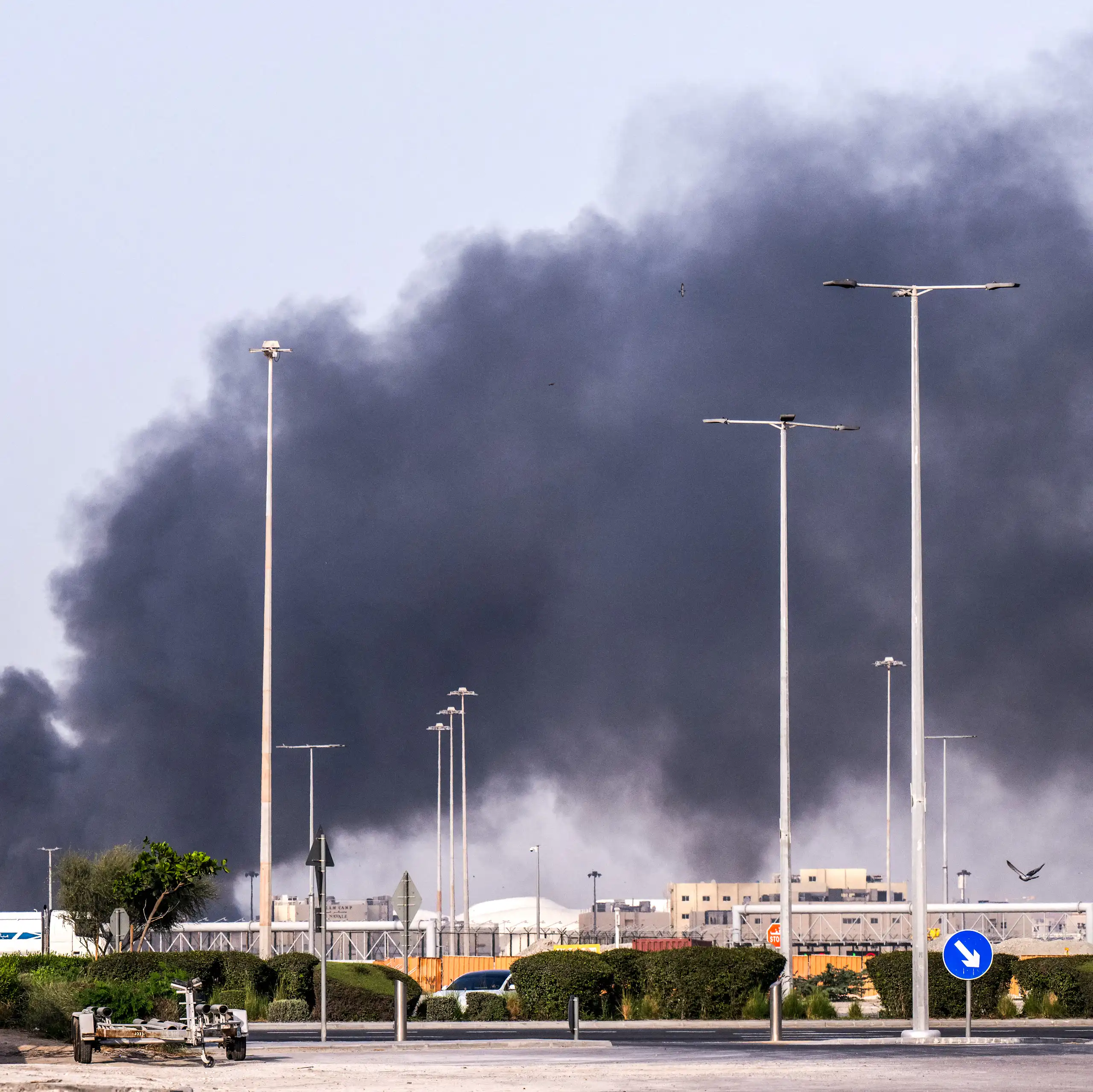 a large plume of black smoke rises in an industrial area