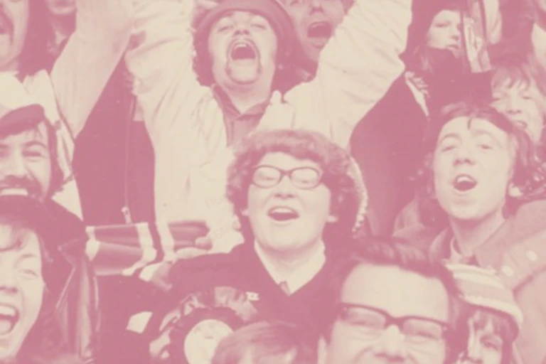 A group of f1970s ootball fans cheering with a happy-looking woman in the middle
