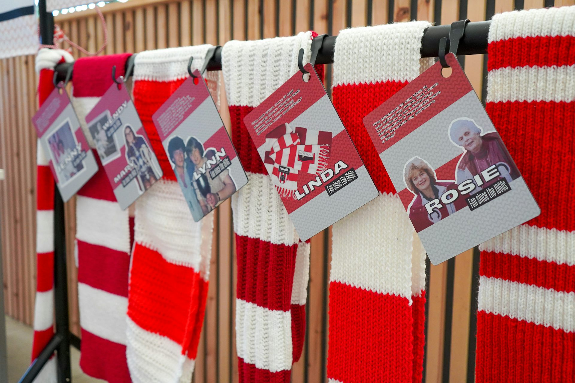 A row of red and white football scarves, each with a woman's name attached.