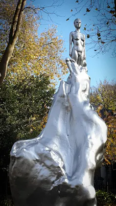 A silver statue of a woman emerging from what a wave