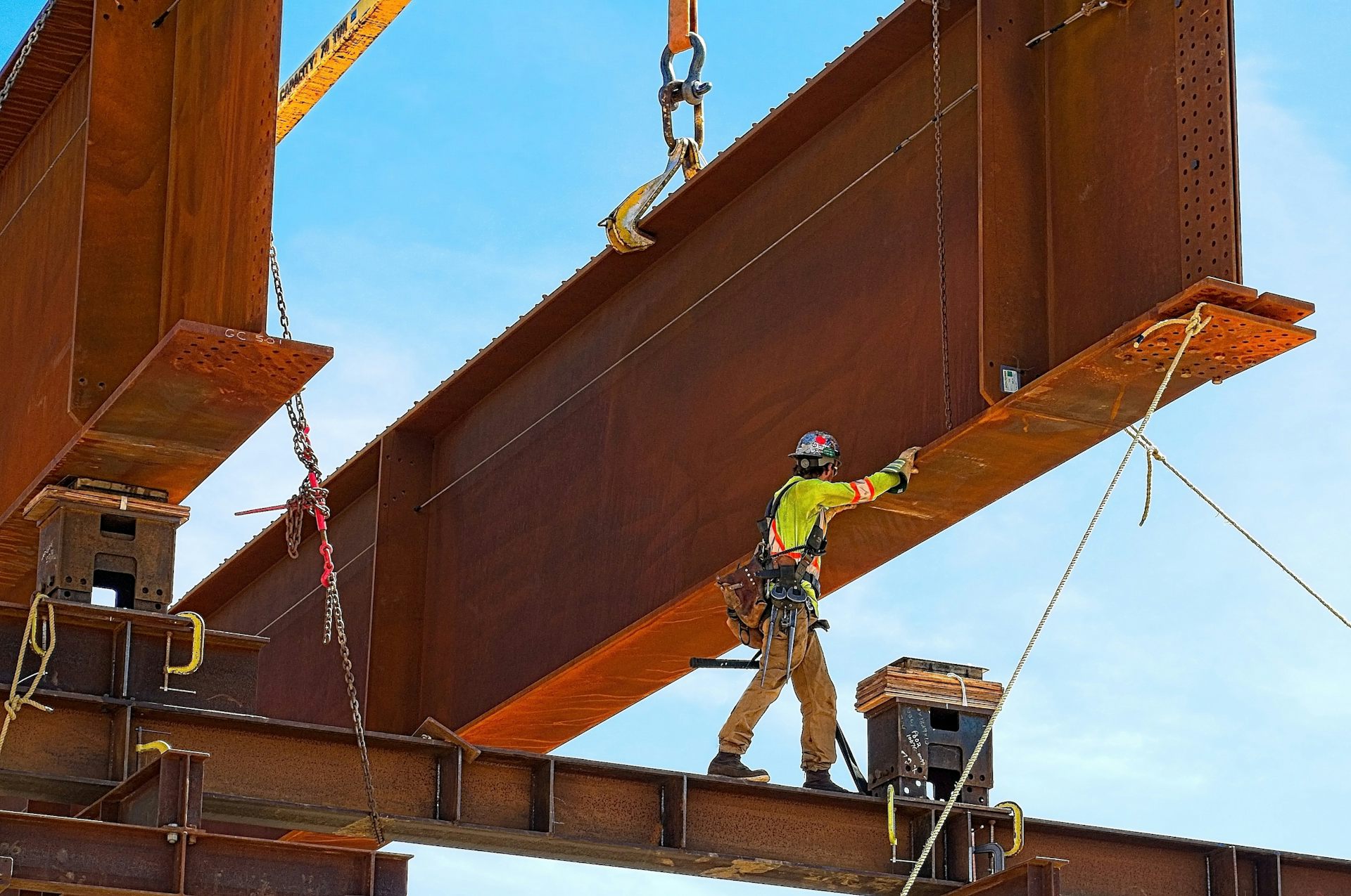 Ouvrier de chantier manipulant une gigantesque structure en métal soulevée par une grue.