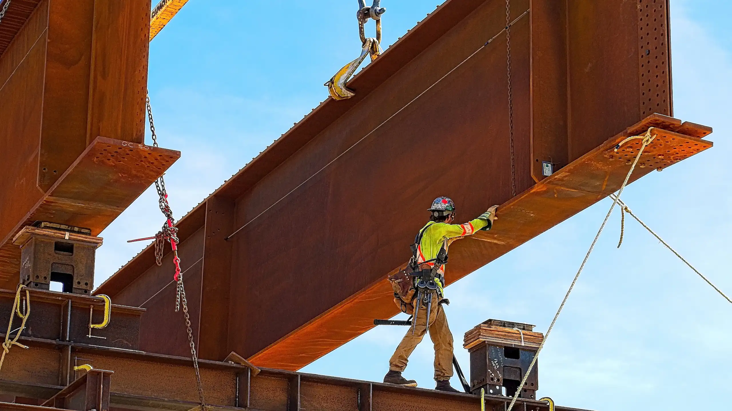 Ouvrier de chantier manipulant une gigantesque structure en métal soulevée par une grue.