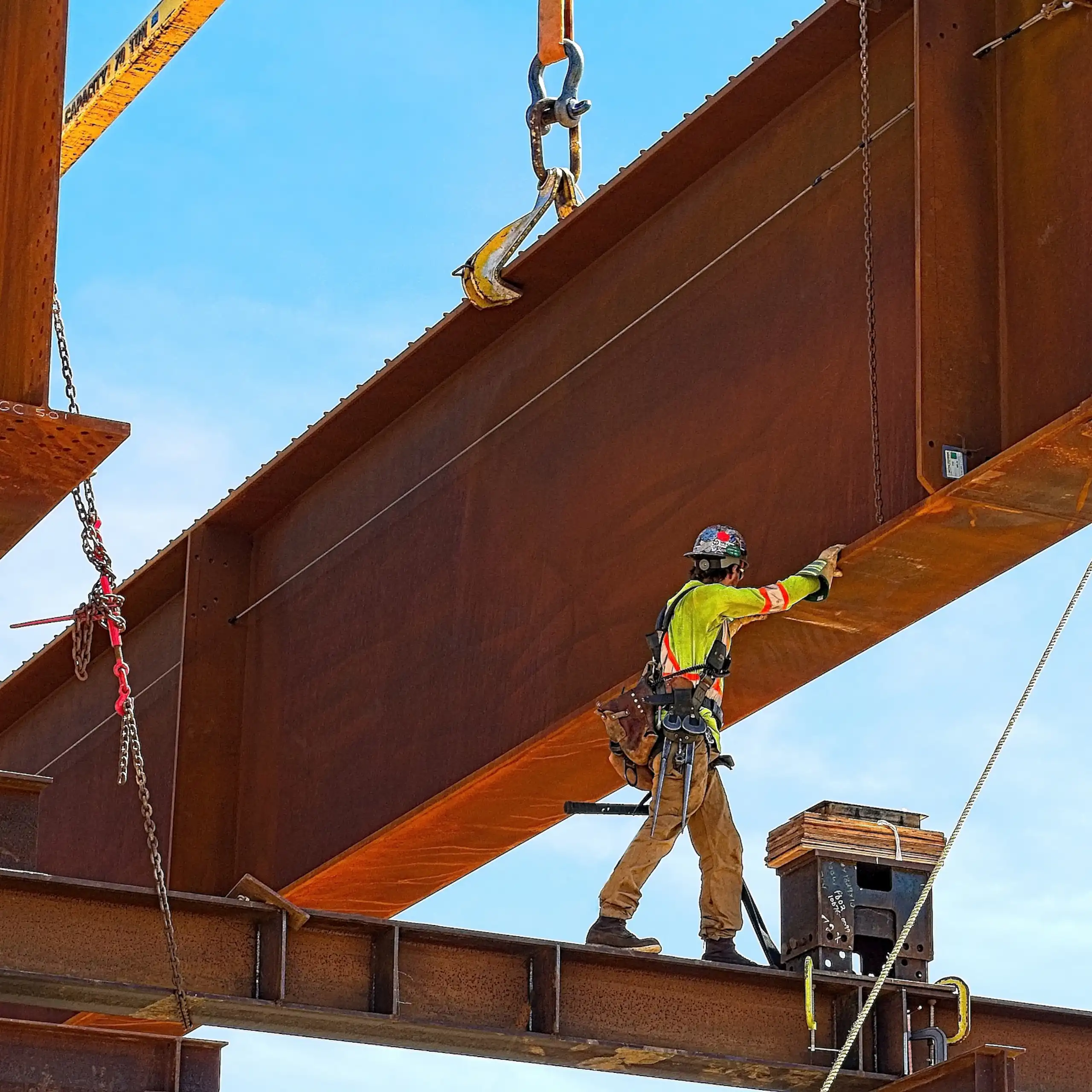 Ouvrier de chantier manipulant une gigantesque structure en métal soulevée par une grue.