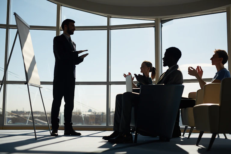man standing at a board presenting to seated colleagues in a high-rise office