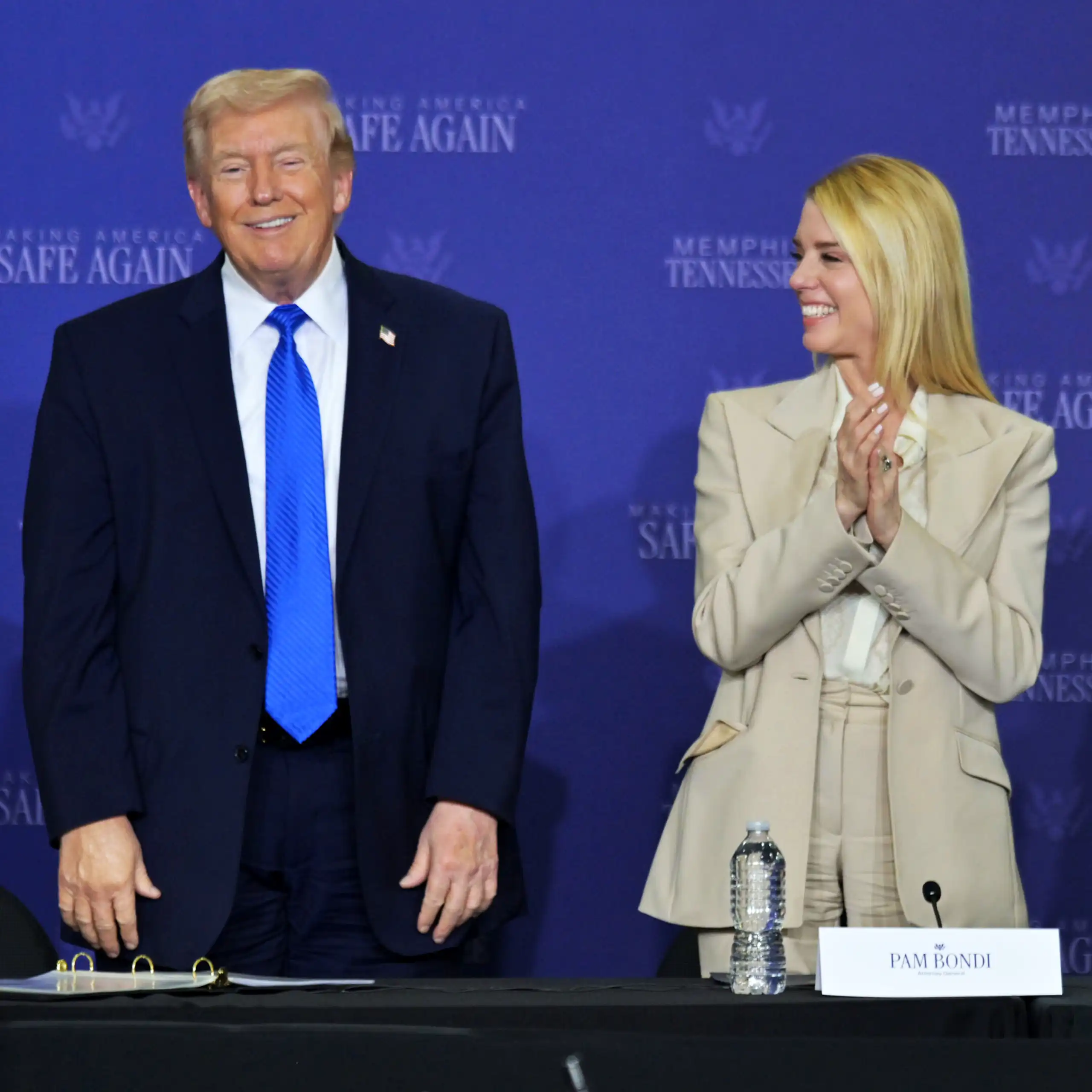 A man dressed in suit and tie stands on a stage next to a woman dressed in a beige suit.