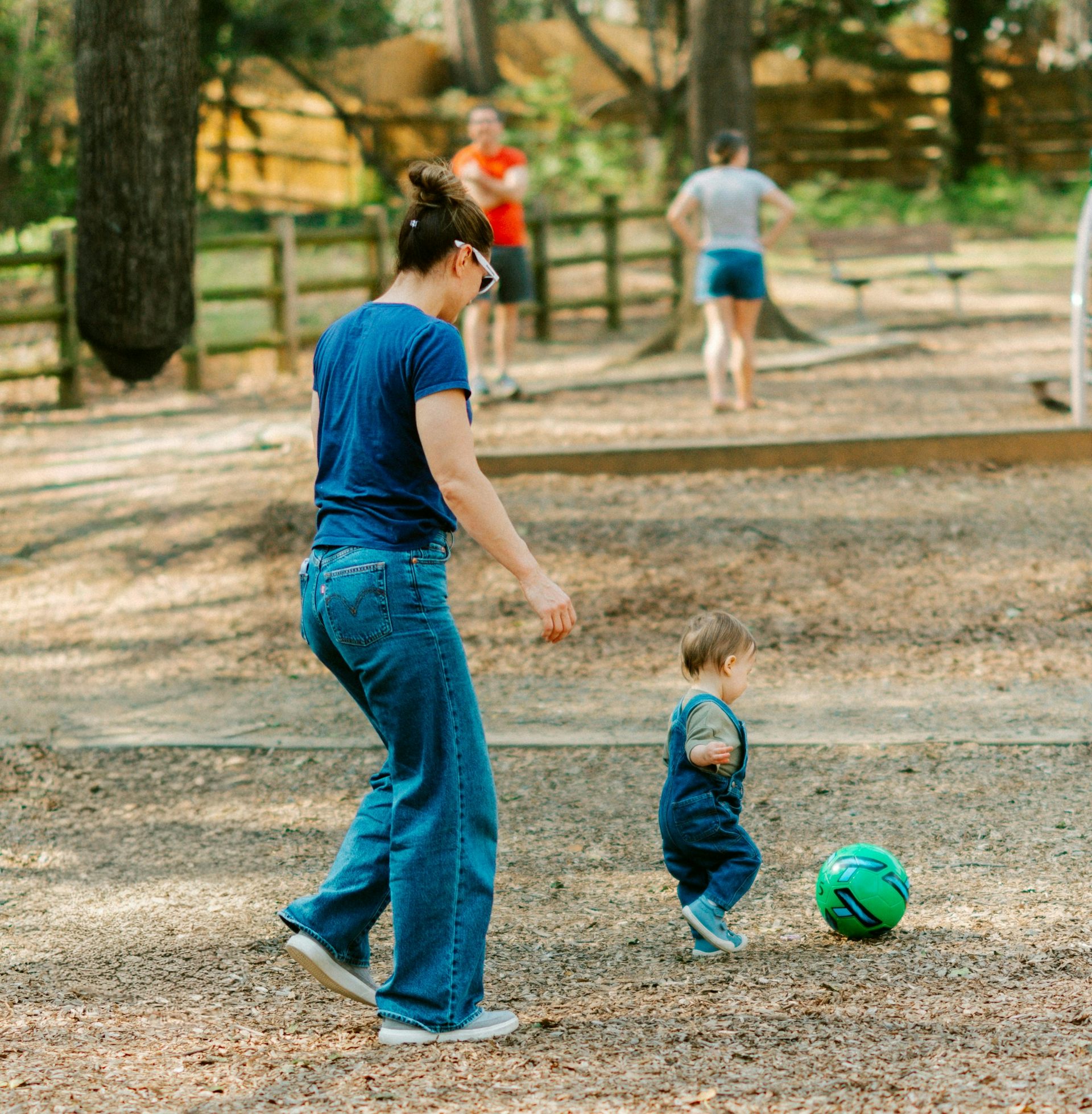Se ve a un padre corriendo detrás de un niño pequeño pateando una pelota.