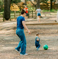 Se ve a un padre corriendo detrás de un niño pequeño pateando una pelota.