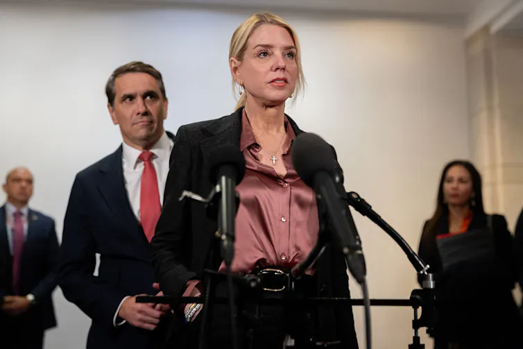 A woman speaks in front of a microphone as a man stands behind her.