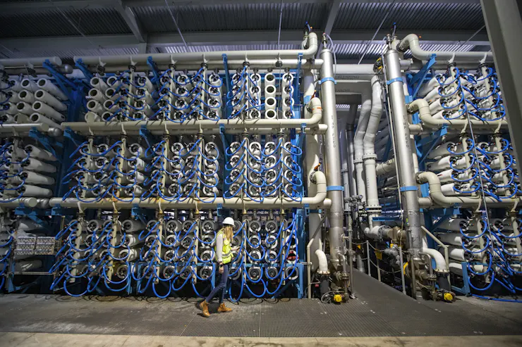 A woman in a hardhat walks past stacks of tubes for making saltwater drinkable.