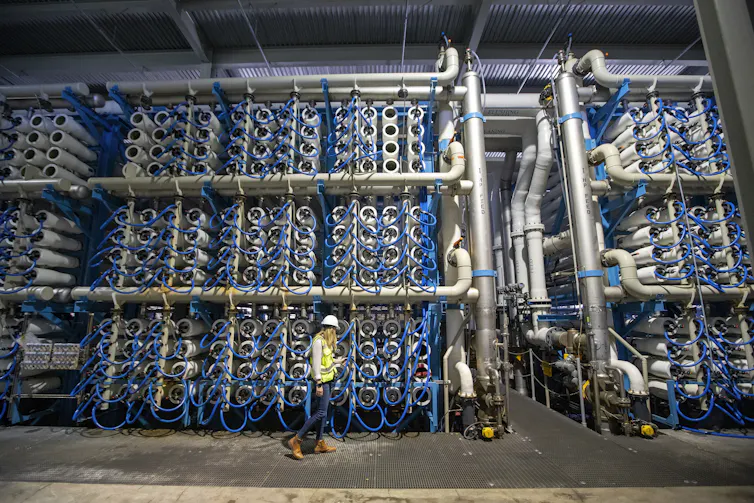 Water conservation works, however local weather alternate is outpacing it: Phoenix, Denver and Las Vegas be offering a glimpse of the long run 1 A woman in a hardhat walks past stacks of tubes for making saltwater drinkable.