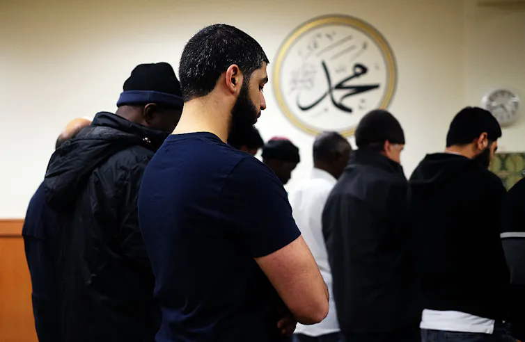Many men stand in rows, praying with their heads bowed.