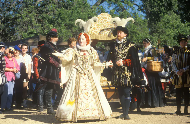 Actors dressed as European royalty from centuries ago perform in front of a crowd of smiling onlookers.