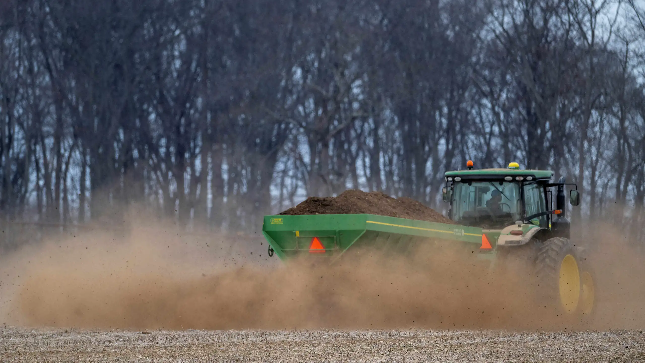 A tractor spreads fertilizer on a field.