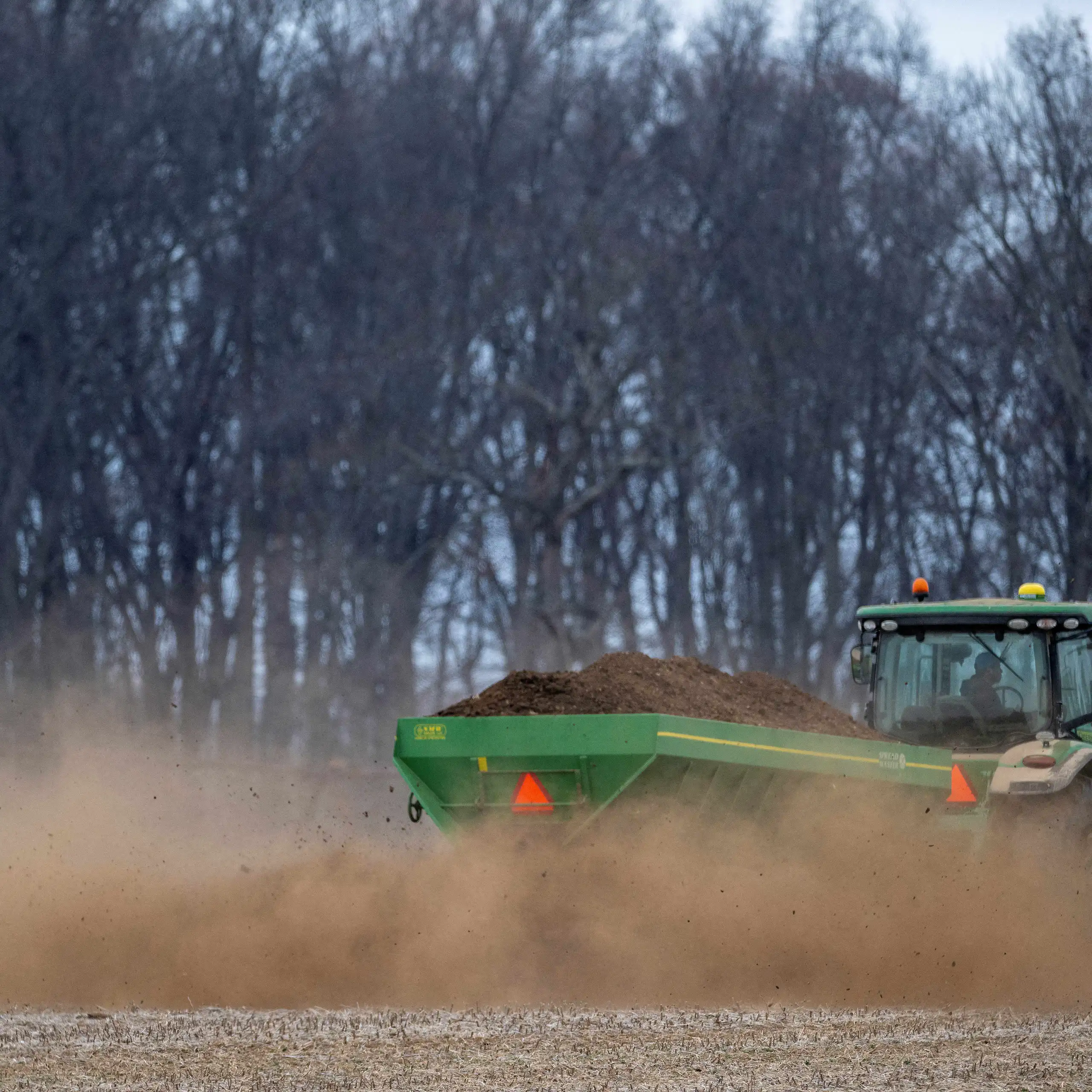 A tractor spreads fertilizer on a field.