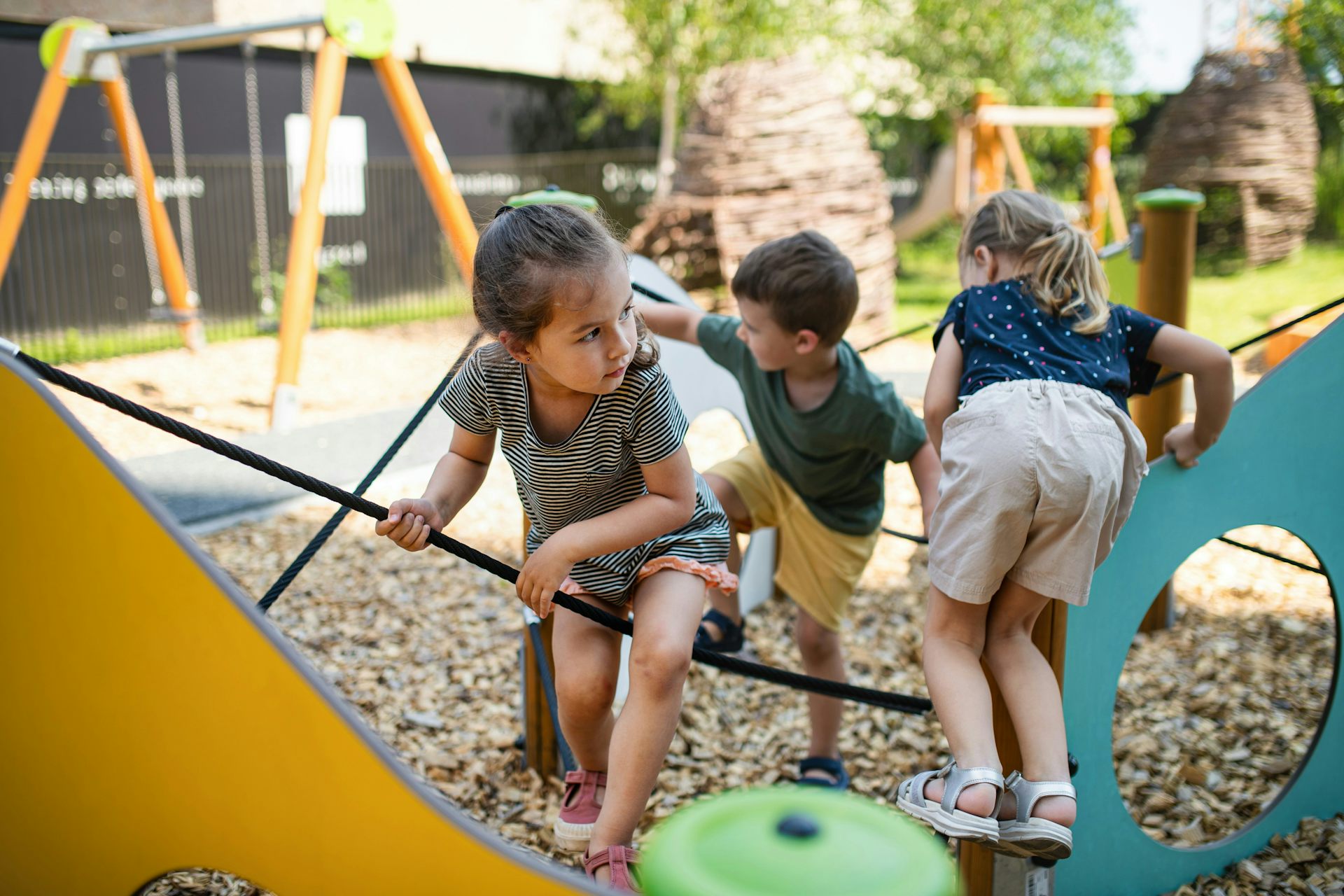 Children climb on a ropes and playground structure outdoors.