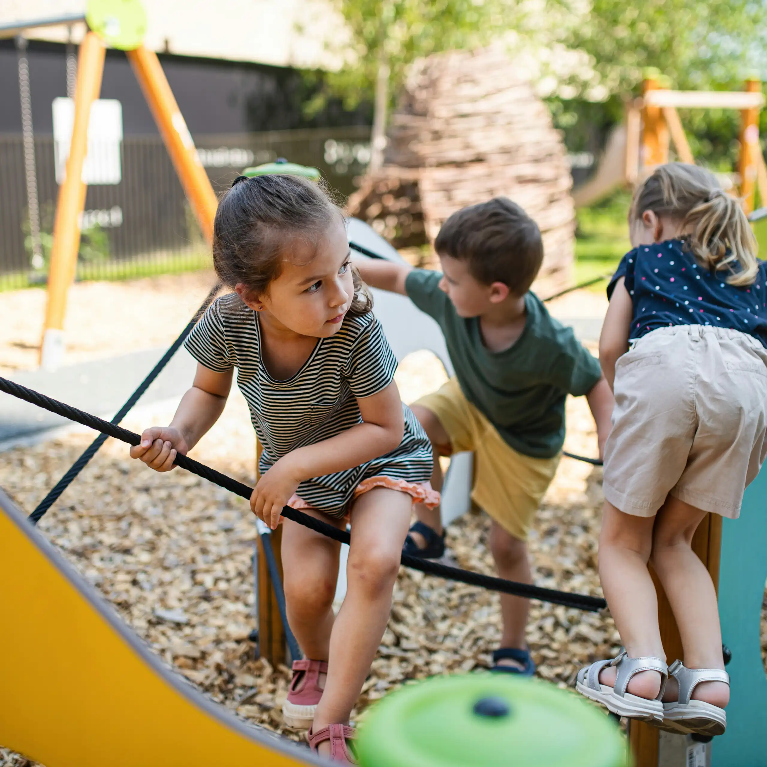 Children climb on a ropes and playground structure outdoors.
