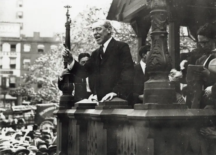 A black and white photo depicts a man outdoors speaking to a crowd.